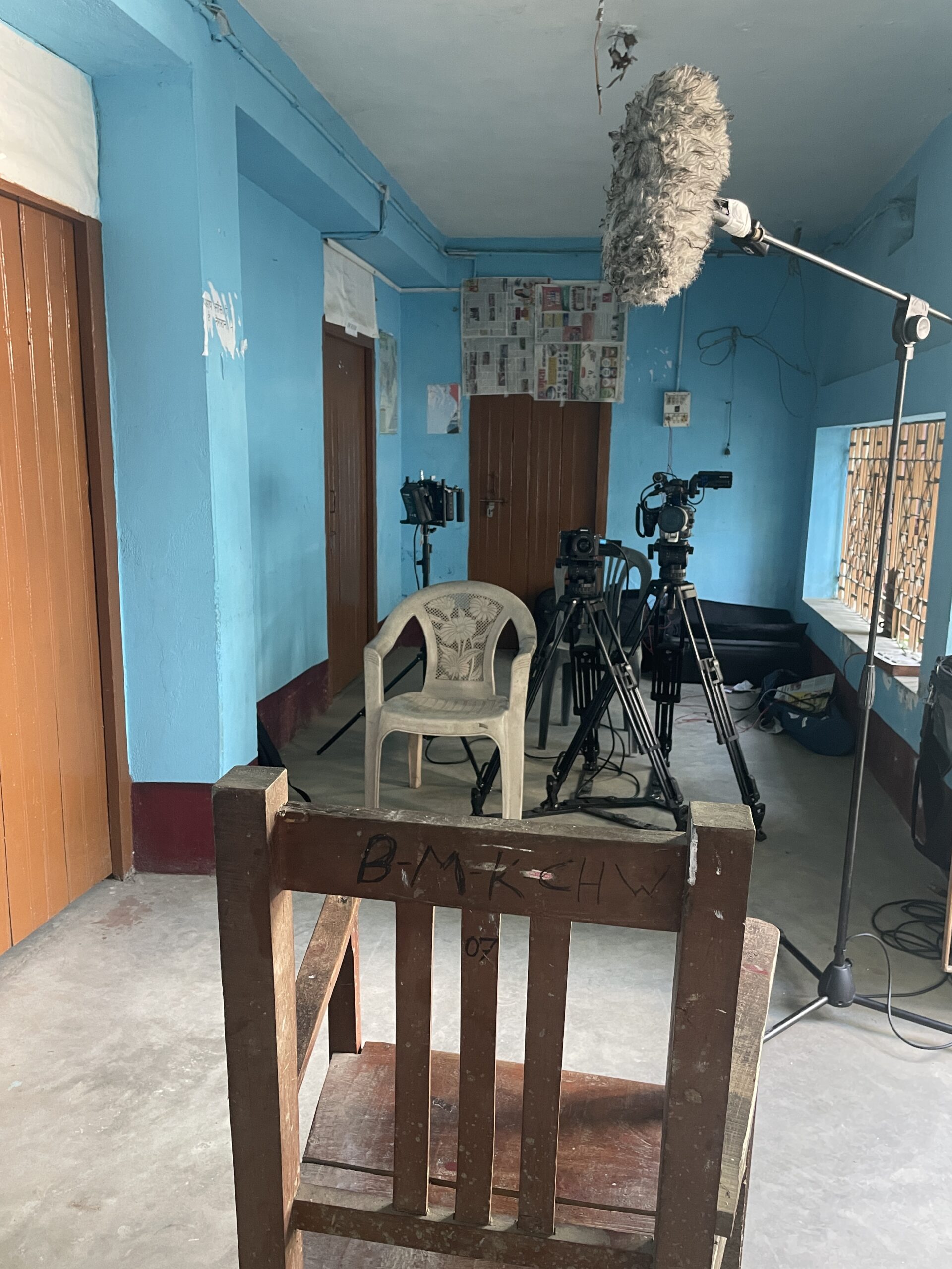 Blue walls, a plastic chair, a wooden chair, camera and mic set-up, awaiting an interview to begin